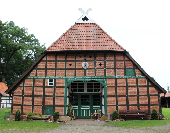 Gehannfors Hof Warmsen Backsteinfachwerkhaus mit rotem Ziegeldach und grüner Holzverzierung vor Wiese und Bäumen.