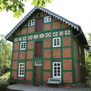 Spieker Lahausen Ein traditionelles Fachwerkhaus mit Ziegelwänden und grünen Akzenten, umgeben von Bäumen und Blumen.