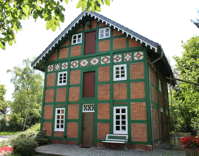 Spieker Lahausen Ein traditionelles Fachwerkhaus mit Ziegelwänden und grünen Akzenten, umgeben von Bäumen und Blumen.