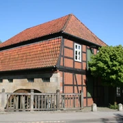 Fachwerkgebäude der Wassermühle Sudweyhe mit rotem Ziegeldach und grünem Laubbaum.