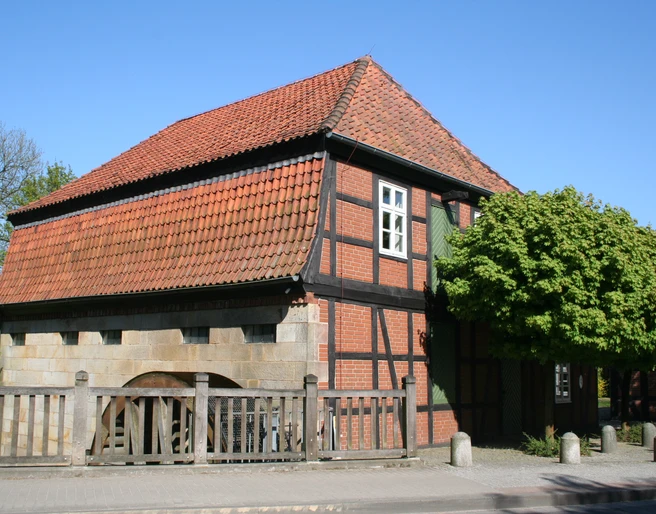 Wassermühle Sudweyhe Fachwerkgebäude der Wassermühle Sudweyhe mit rotem Ziegeldach und grünem Laubbaum.