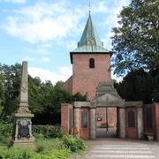 Marienkirche Leeste Backsteinkirche mit grünem Turmhelm, umgeben von Bäumen, daneben ein historischer Obelisk.