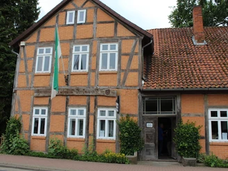 Heimatmuseum Rodewald Fachwerkhaus mit Backsteinmauern und blühenden Pflanzen. Eingangstür geöffnet, grüne Fahne weht.