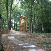 Rathauspark Achim Spielplatz im Rathauspark Achim mit Holzspielgeräten, umgeben von Bäumen und einem gepflasterten Weg.