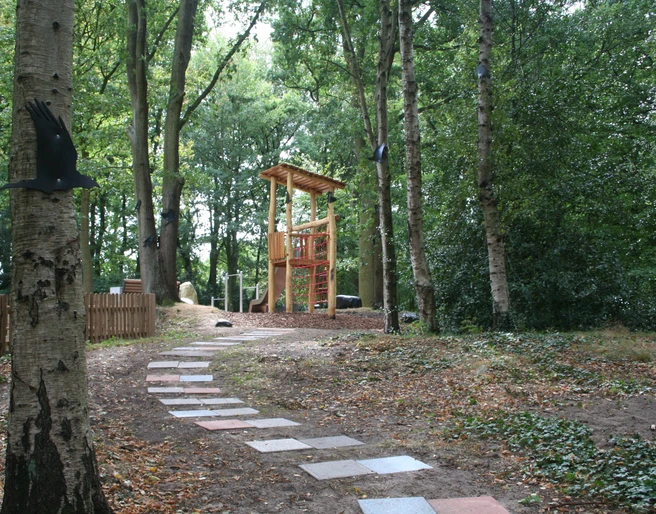 Rathauspark Achim Spielplatz im Rathauspark Achim mit Holzspielgeräten, umgeben von Bäumen und einem gepflasterten Weg.