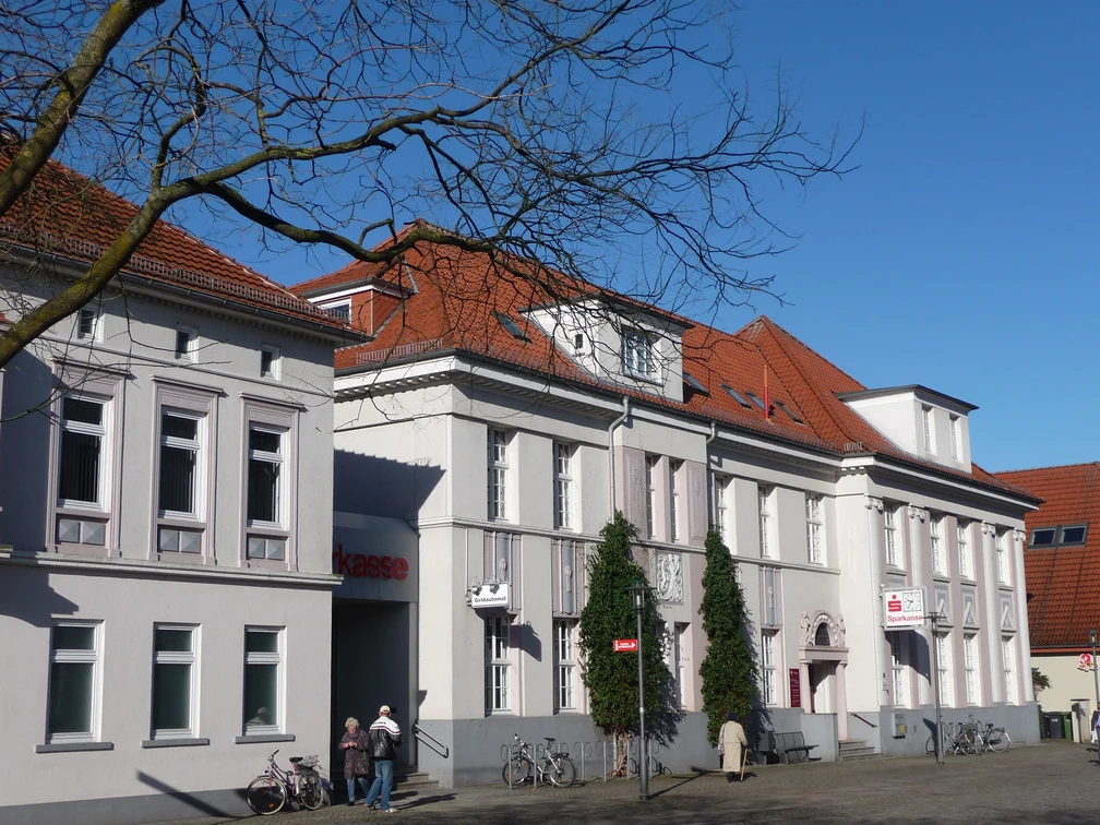 Sparkassengebäude Achim Historisches weißes Gebäude mit rotem Ziegeldach, Sitz der Sparkasse in Achim, Bäume im Vordergrund.