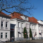 Sparkassengebäude Achim Historisches weißes Gebäude mit rotem Ziegeldach, Sitz der Sparkasse in Achim, Bäume im Vordergrund.