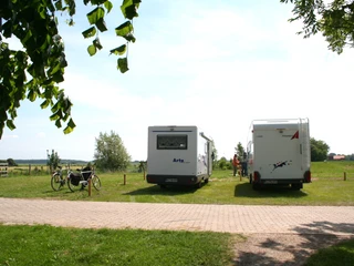 Wohnmobilstellplatz Hoya Zwei Wohnmobile stehen auf einer grünen Wiese in Hoya, mit Fahrrädern und weitem Blick auf die Landschaft.