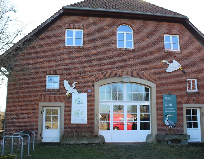 Ein historisches Backsteingebäude mit großen Fenstern und Tierfiguren an der Fassade, umgeben von Bäumen.