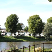 Reisemobilstellplatz Nienburg Reisemobilstellplatz an Flussufer mit Wohnmobilen im Hintergrund und Bäumen im Vordergrund.