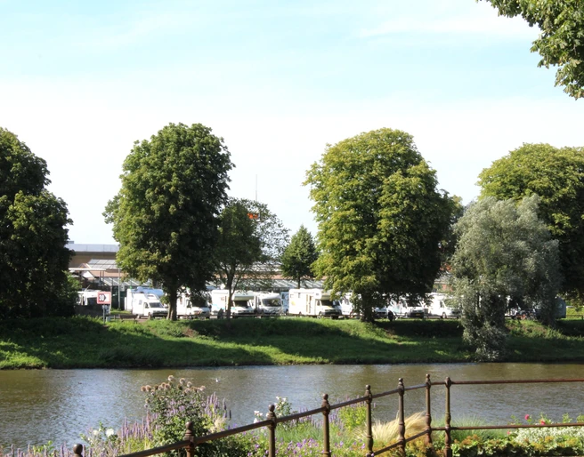 Reisemobilstellplatz Nienburg Reisemobilstellplatz an Flussufer mit Wohnmobilen im Hintergrund und Bäumen im Vordergrund.
