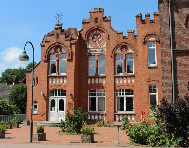 Bauschule Rehburg Backstein-Gebäude der Bauschule Rehburg mit imposanter Fassade und verzierten Fensterbögen bei Sonnenschein.