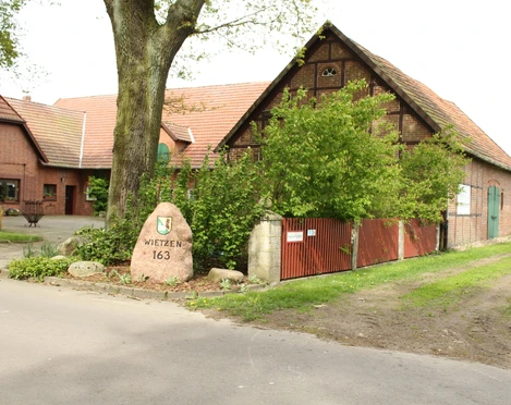 Unser kleiner Hof Wietzen Ein alter Bauernhof mit Backsteingebäuden, umgeben von grünen Bäumen und einem Weg aus Asphalt.