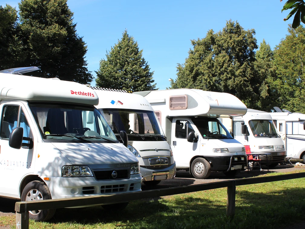 Wohnmobilstellplatz Reihen abgestellter Wohnmobile auf einem Stellplatz, umgeben von Bäumen bei klarem Wetter.