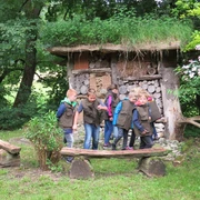 Insektenhotel am Waldhaus Durbeke bei Altenbeken Kinder in grünen Westen erkunden ein mit Holz und Naturmaterialien gefülltes Insektenhotel im Wald.