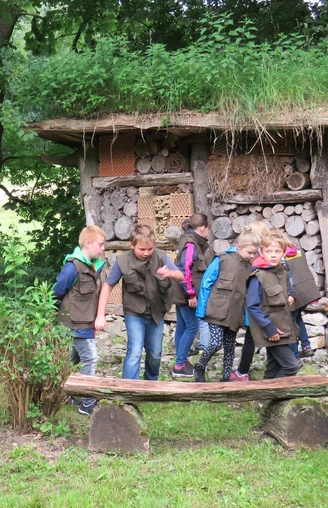 Insektenhotel am Waldhaus Durbeke bei Altenbeken Kinder in grünen Westen erkunden ein mit Holz und Naturmaterialien gefülltes Insektenhotel im Wald.