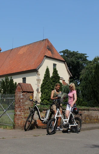 Kirche Eystrup Zwei Fahrradfahrerinnen im Gespräch vor der historischen Kirche Eystrup mit markantem Turm.