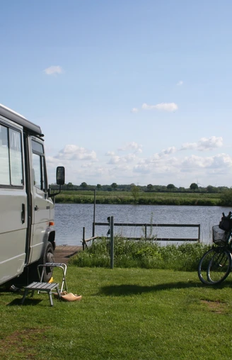 Wohnmobil steht auf einer Wiese am See, neben zwei Fahrrädern und einem Stuhl mit Blick aufs Wasser.
