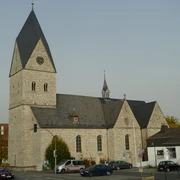 Historische Kirche mit hohem Turm, grauem Steinmauerwerk und einem Uhrziffernblatt über der Kreuzung.