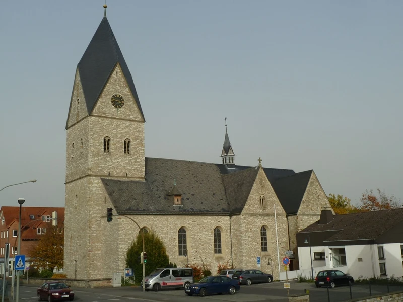 Historische Kirche mit hohem Turm, grauem Steinmauerwerk und einem Uhrziffernblatt über der Kreuzung.