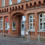 Tourist-Information Nienburg Rotes Backsteingebäude mit hohen Fenstern und Eingang zur Tourist-Information Nienburg an der Straße.