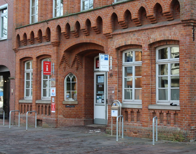 Tourist-Information Nienburg Rotes Backsteingebäude mit hohen Fenstern und Eingang zur Tourist-Information Nienburg an der Straße.