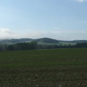 Blick von der Egge Weite grüne Felder erstrecken sich vor sanften Hügeln unter einem leicht bewölkten Himmel.