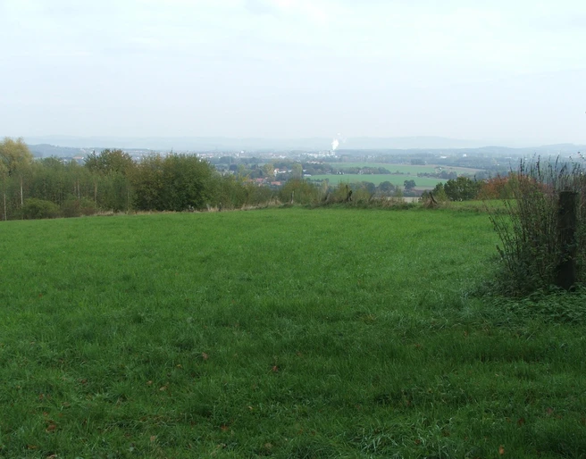 Blick nach lage Weite grüne Wiese mit Blick auf eine ferne Stadtlandschaft unter bewölktem Himmel.