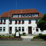 Das weiße, zweistöckige Rathaus von Bad Wünnenberg mit roten Dachziegeln und blühenden Blumenkästen.