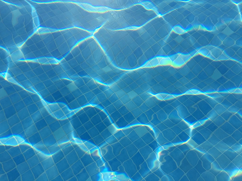 Schwimmbecken Klares, blaues Wasser eines Schwimmbeckens mit sanften Lichtreflexionen auf gefliester Oberfläche.
