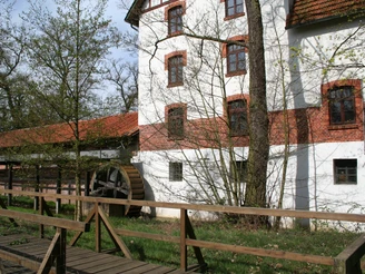 Historische Wassermühle mit rustikalem Ziegelbau, Holzwasserrad und umliegenden grünen Bäumen.