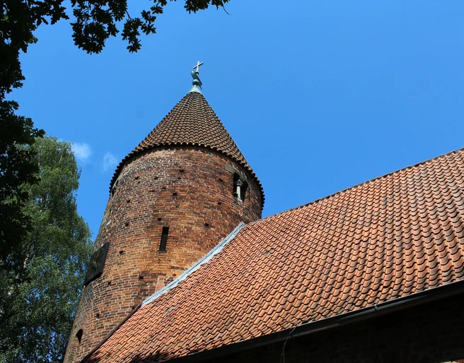 Kirche St. Annen Westen Backsteinkirche mit markantem Rundturm und Schieferdach, umgeben von Bäumen und blauem Himmel.
