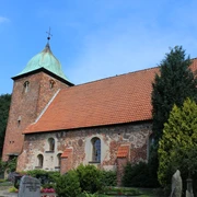 Historische Backsteinkirche mit markantem Turm und begrüntem Umfeld unter blauem Himmel.