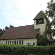 Kirche Essern Kirche in Essern mit markantem Glockenturm, umgeben von Bäumen und von einer Hecke eingefasst.
