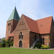 Kirche Riede Backsteinkirche mit grünem Turmdach, Satteldächern und gepflegtem Grün vor blauem Himmel.