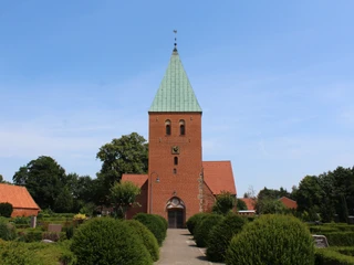 Historische Backsteinkirche mit grünem Turmdach, umgeben von gepflegter Gartenlandschaft.