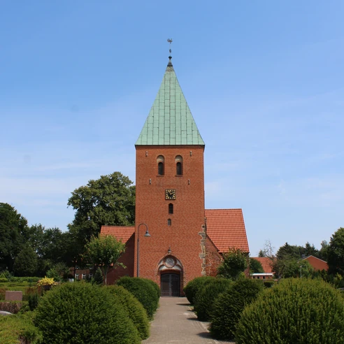 Kirche Riede Historische Backsteinkirche mit grünem Turmdach, umgeben von gepflegter Gartenlandschaft.
