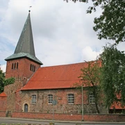 Backsteinkirche mit markantem Spitzdach, umgeben von Bäumen, vor bewölktem Himmel in Holtorf.