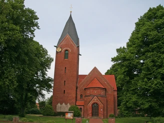 Alte Kapelle Schweringen Backstein-Kapelle mit hohem Turm und Uhr, umgeben von grünen Bäumen unter einem bewölkten Himmel.