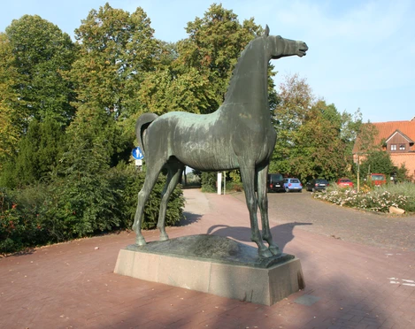 Wiehender Hengst Bronzestatue eines aufrecht stehenden, wiehenden Hengstes auf einem gepflasterten Platz, umgeben von Bäumen.