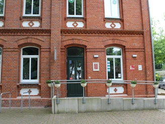 Tourist-Info Stolzenau Rotes Backsteingebäude der Tourist-Info Stolzenau mit barrierefreiem Eingang und Blumenkübeln.