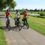 Drei Radfahrer genießen eine sonnige Fahrt auf einem Radweg entlang der grünen Weserlandschaft.