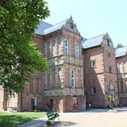Schloss Erbhof Historisches Backsteinschloss mit grüner Umgebung und blauen Türen, beleuchtet von sommerlichem Sonnenlicht.