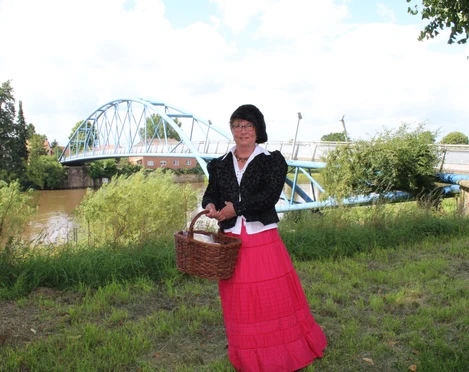 Gewandete Stadtführerin Nienburg Eine Stadtführerin in historischer Kleidung steht mit einem Korb an der Weserbrücke in Nienburg.