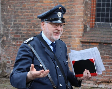 Gewandeter Gästeführer Nienburg Ein Gästeführer in historischer Polizeiuniform spricht gestikulierend vor einer Backsteinwand.