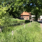 Historische Klostermühle Heiligenberg aus Backstein an einem ruhigen Waldweg und Teich im Sommer.