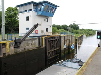 Schleuse Langwedel Schleuse Langwedel am Weserfluss mit modernem Kontrollturm und einem Frachtschiff auf ruhigem Wasser.