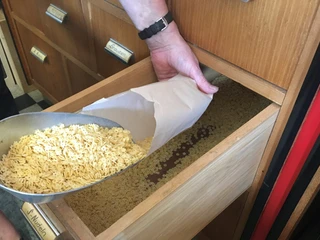 Tante Emma Neuenkruge Nudeln.jpg Eine Hand füllt vorsichtig Nudeln aus einer großen Schaufel in eine offene Schublade.