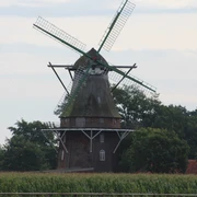 Sprakener Windmühle in Schwarme Historische Windmühle in Schwarme, umgeben von Bäumen und einem Weizenfeld, unter wolkigem Himmel.