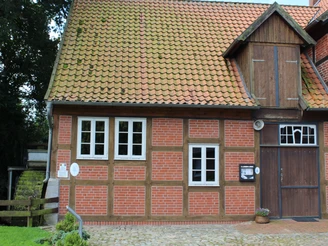 Wassermühle Bruchmühlen Fachwerkgebäude mit roten Ziegelwänden und Holztor, daneben drei weiße Fenster. Links ein Holzbalken.